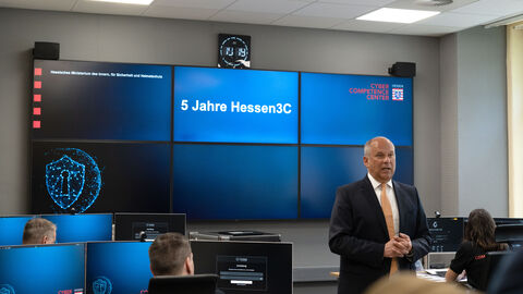 Innenmister Roman Poseck steht vor einer blauen Monitorwand im Hessen3C.